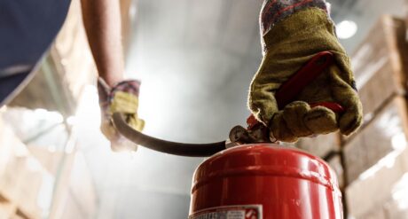 A man with an understanding of fire safety fundamentals carries a fire extinguisher in a warehouse